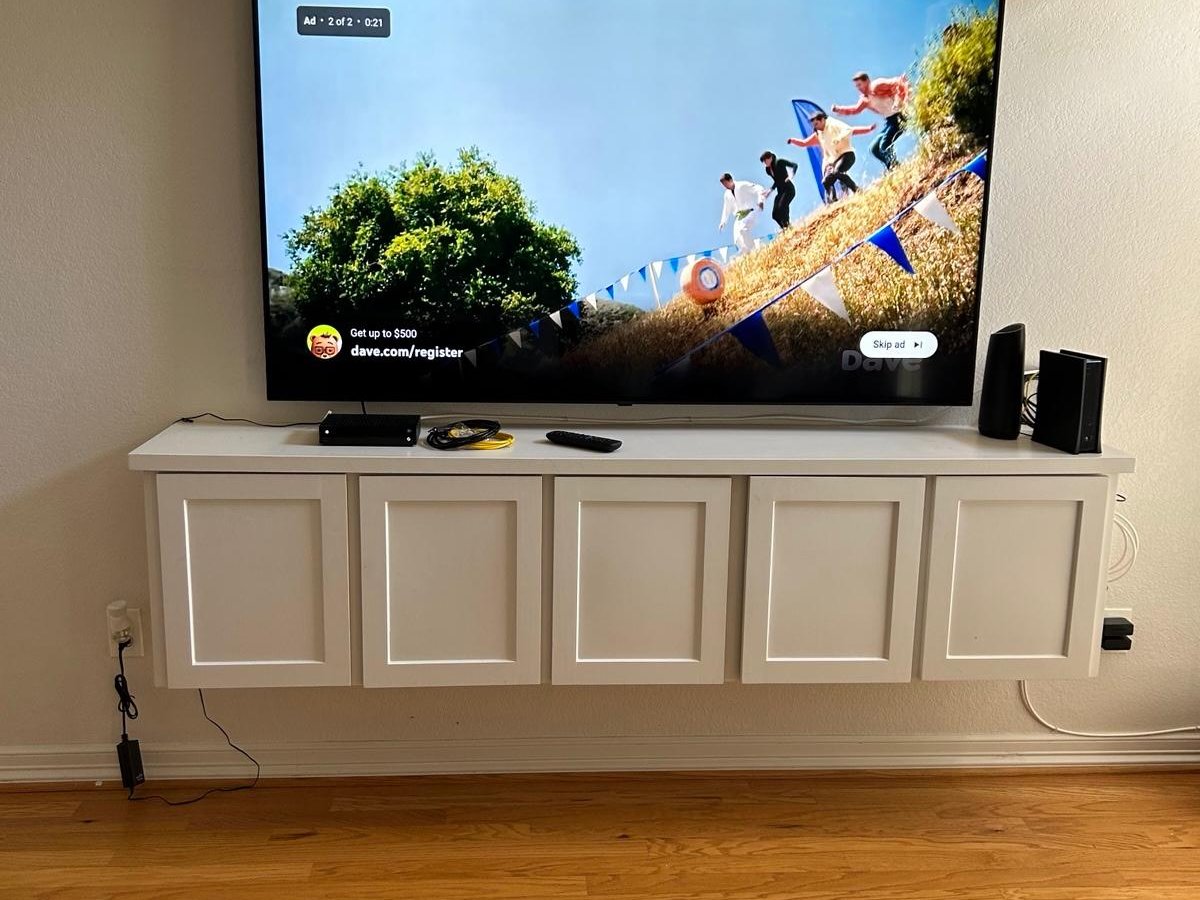 TV mounted on wall above a floating shelf cabinet